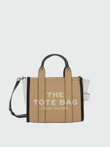 Cartera tipo tote bag Marc Jacobs en color tostado, con detalles en negro y blanco. Cuenta con las inscripciones "THE TOTE BAG" y "MARC JACOBS" estampadas en el frente. Posee doble asa de mano superior y correa de hombro ajustable y desmontable.