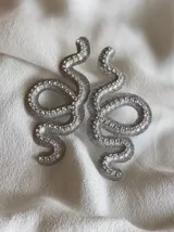 Par de aros colgantes con forma de serpiente contorneada en strass, con sistema de cierre a presión de acero inoxidable.