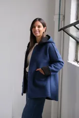 Tapado de paño azul con capucha, diseño de corte holgado y largo a la cadera. Presenta detalles en color negro en el interior, bordes y puños, con bolsillos frontales amplios y cierre frontal.