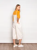 Mono de jean color crudo, de corte holgado, con pierna ancha y largo cropped. Tiene tirantes finos y un bolsillo cuadrado en el pecho.