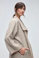 Tapado de largo medio abierto con cuello, confeccionado en lana fina sin teñir con detalles de terminación envivados en los bordes y mangas tres cuartos.