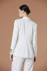 Saco tipo blazer de Natalia Antolín, color blanco, con solapas de satén en contraste, cierre frontal con un botón y detalle de parche con logo en la manga.