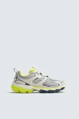 Zapatilla deportiva tipo running color blanco hueso con detalles en azul marino y amarillo flúor.