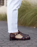 Sandalias estilo romano de cuero marrón oscuro, con diseño de tiras entrelazadas, talón cerrado y hebilla metálica de ajuste lateral.