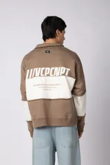 Buzo tipo polo de calce relajado con diseño de bloques de color en tonos marrón y blanco. Presenta cuello polo, cierre frontal parcial y logo estampado en el pecho. Confeccionado en tejido pesado con estructura.