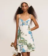Vestido corto de corte evasé confeccionado en tejido laise con estampa tropical de flores azules y hojas verdes. Presenta escote en V, breteles finos ajustables y diseño con perforaciones caladas características del broderie.