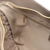 Cartera tipo tote de diseño curvo, confeccionada en cuero sintético color gris. Presenta asas regulables con hebillas metálicas y un aplique triangular metálico con el logo de la marca en el frente.