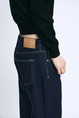 Jeans de tiro medio confeccionados en denim azul oscuro, con diseño de cinco bolsillos, trabillas para cinturón y bajo deshilachado. Cierre frontal con cremallera y botón metálico.