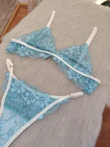 Conjunto de lencería compuesto por un corpiño triangular y una bombacha, confeccionados en encaje floral color aguamarina con detalles de ribetes en color champagne. El corpiño cuenta con breteles regulables y la bombacha presenta laterales ajustables.