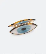 Pinza para el pelo de tamaño mediano con diseño en forma de ojo. Presenta un estampado de iris azul sobre fondo blanco y detalles en carey en los bordes.