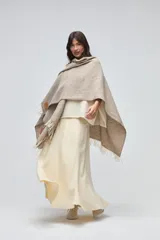 Ruana de lana sin teñir en tono beige, con textura tejida y terminaciones con flecos en los bordes.