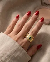 Anillo ancho de bronce con baño de oro, diseño texturizado con detalles ornamentales, piedra central verde ovalada rodeada de circonias y pequeñas piedras rojas incrustadas.