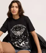 Remera negra de algodón con cuello redondo y manga corta. Presenta un estampado grande en blanco con temática mística que incluye una polilla con diseño de calavera, estrellas, lunas y montañas, y la frase "dream culture in mystic haven".
