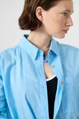 Camisa de algodón color beige, de corte holgado y diseño oversize, con cuello camisero, mangas largas, bolsillo frontal y cierre de botones de madera.