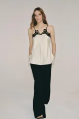 Top de tejido satinado color crema con escote en pico y tirantes finos. Presenta detalles de encaje negro en contraste en el escote y bajo recto.
