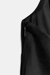 Chaleco estilo halter con escote en pico profundo, confeccionado en tejido efecto ante. Presenta detalle de tachas metálicas a lo largo de los bordes frontales y cierre mediante lazada en la nuca.