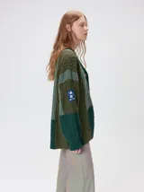 Cardigan oversize de tejido de punto grueso con diseño de bloques de color en tonos tierra. Presenta cuello en V, cierre frontal con botones, mangas largas con terminación abullonada y parches decorativos en el pecho y hombro.