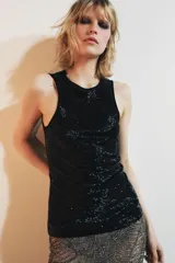 Top negro sin mangas, con cuello redondo y abertura con botón en la espalda. Presenta un detalle de abalorios a tono en el borde del cuello y sisas.