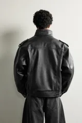 Cazadora biker relaxed fit confeccionada en tejido efecto piel, color negro. Cuenta con cuello subido, manga larga con puño ajustable y bajo elástico. Incluye bolsillos de vivo en la cadera y cierre frontal con cremallera oculta bajo una solapa diagonal con botones a presión.