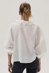 Blusa blanca con lunares en relieve, cuello con volados y lazos, mangas abullonadas 3/4 y bordados con lentejuelas en el frente.