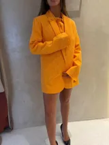 Blazer de corte sastre en color naranja, con solapas clásicas y manga larga. La prenda presenta un acabado texturizado con incrustaciones de strass en toda su superficie, aportando un brillo sutil y sofisticado.