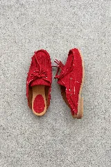 Zuecos de cuero gamuzado color rojo con diseño marinero, flecos frontales, cordones decorativos y suela plana.