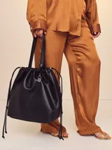 Bolso tipo tote color negro de cuero sintético ultrasuave, con silueta relajada, cordón ajustable en la parte superior y asas superiores.