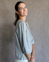 Blusa de crepe color gris claro, con mangas tres cuartos que presentan cortes y pespuntes decorativos. Posee un diseño holgado y cuello redondo.