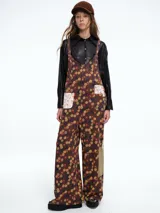 Mono de corte holgado con estampado floral sobre fondo marrón. Presenta tirantes ajustables, bolsillos frontales con parches en contraste y diseño de pierna ancha.