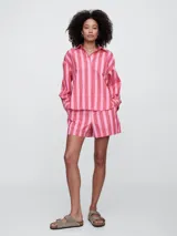 Camisa de corte oversize confeccionada en popelina, con diseño de rayas verticales en tonos verde y blanco. Presenta cuello clásico, cierre frontal con botones y bolsillo en el pecho.