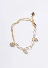 Pulsera de cadena doble con eslabones ovalados texturizados, bañada en oro 18k sobre base de plata 925. Presenta tres dijes colgantes en forma de corazón decorados con zirconias brillantes.