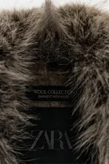 Chaqueta de corte recto confeccionada en mezcla de lana, color marrón topo. Presenta un cuello de solapa amplio con aplicación de pelo sintético desmontable, cierre frontal cruzado con botones y bolsillos laterales con solapa.