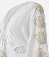 Vestido corto de playa confeccionado en voil de algodón BCI color blanco, con escote en V con lazo, cutouts laterales, mangas largas y bordados de caracoles de mar.