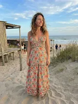 Vestido largo con escote en V, sin mangas y cintura marcada. Presenta un estampado de diseño geométrico y floral con detalles en tonos terracota, crema y azul.