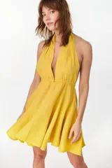 Vestido corto color amarillo de lino italiano, con escote halter cruzado en V pronunciado y cintura elastizada fruncida con falda amplia y voluminosa.