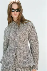 Chaqueta cruzada de estructura en tejido tweed de mezcla de hilos en tonos blanco y negro, con escote en pico, manga larga y cierre frontal con botones a presión ocultos.