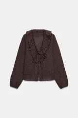 Camisa de manga larga con estampado de cuadros, escote en pico con volantes decorativos y cierre frontal con botones. Presenta puños elásticos.
