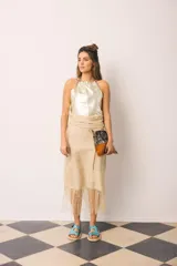 Falda midi color beige de tiro alto y silueta envolvente, con lazo ancho para anudar en la cintura, diseño asimétrico y terminación de flecos largos en el ruedo.