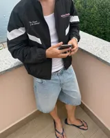 Campera deportiva negra con cuello alto, cierre frontal completo y diseño oversize. Cuenta con bandas blancas diagonales en las mangas y el torso, y texto estampado en el pecho.