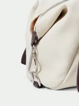 Cartera tipo shoulder bag de diseño cilíndrico, confeccionada en material sintético color crema con textura. Presenta correas largas ajustables en color marrón oscuro con detalles de hebillas y ojalillos metálicos.