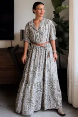Vestido largo de diseño amplio en tono gris con estampado estilo paisley, cuello camisero con volados y mangas cortas abullonadas. Cuenta con falda larga con volado en el borde inferior.