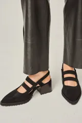 Zapato cerrado de cuero negro, con punta fina, taco ancho y plataforma con suela de goma dentada. Presenta tiras de sujeción cruzadas en el empeine y una tira elástica en el talón.