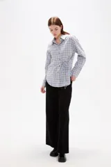 Camisa de poliéster con estampado a cuadros, cuello camisero, cierre frontal con botones y detalle de lazo ajustable en la cintura.