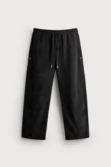 Pantalón jogger de corte relajado en color negro, confeccionado en tejido con elasticidad. Presenta cintura elástica con cordón ajustable y bolsillos laterales decorados con tachas metálicas.