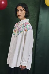 Camisa de corte oversize con mangas largas y puños abotonados. Presenta un diseño bicolor con cuerpo blanco y un canesú delantero con estampado floral multicolor.