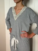 Pijama de algodón gris con textura acanalada, compuesto por una remera de escote en V decorado con puntilla y un pantalón recto con elástico y lazo en la cintura.