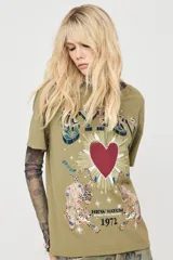 Remera verde militar de manga corta, con cuello redondo y diseño holgado. Presenta una estampa frontal con la palabra "GYPSY", un corazón rojo rodeado de rayos y dos leopardos acompañados de detalles decorativos y tipografía estilo vintage.