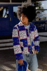 Campera corta con estampado floral en tonos azules, rojos y amarillos sobre fondo blanco. Diseño capitoneado a mano en 100% algodón, con cuello camisero, broches metálicos y bolsillos plaqué.