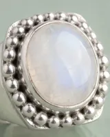 Anillo de plata 925 con piedra de la luna central de forma ovalada, rodeada por un marco de pequeñas esferas metálicas.