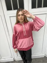 Canguro oversize de plush color rosa viejo, con capucha, mangas globo con puños fruncidos y bolsillo frontal tipo canguro. Presenta tajos laterales con tiras ajustables y cordones en la capucha.